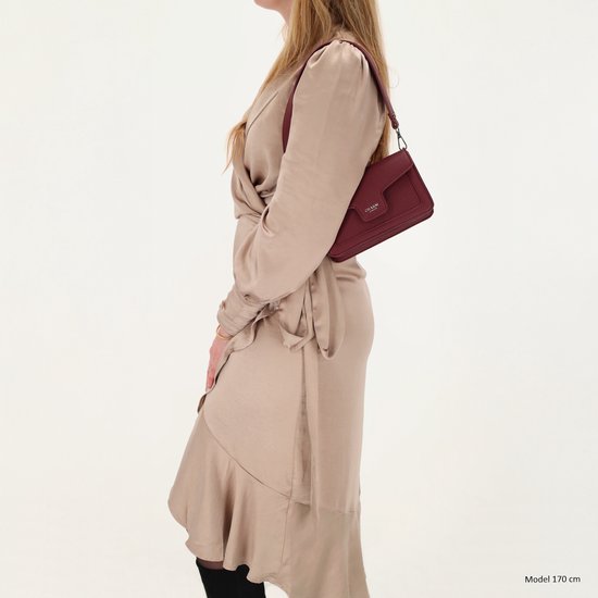 Model draagt bordeauxrode schoudertas, zij-aanzicht, over een beige jurk.