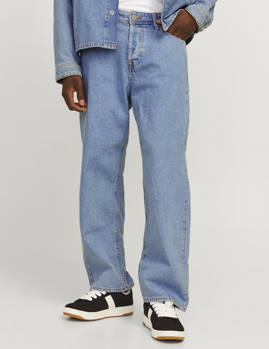Detail van de benen van een man in een denim jack en jeans met sneakers.