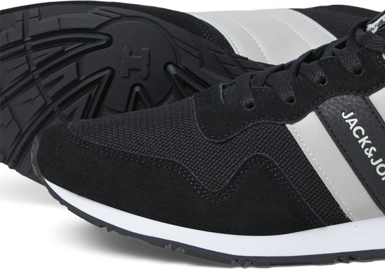 Close-up van een zwarte sneaker met witte en grijze strepen, witte zool en zwarte buitenzool.