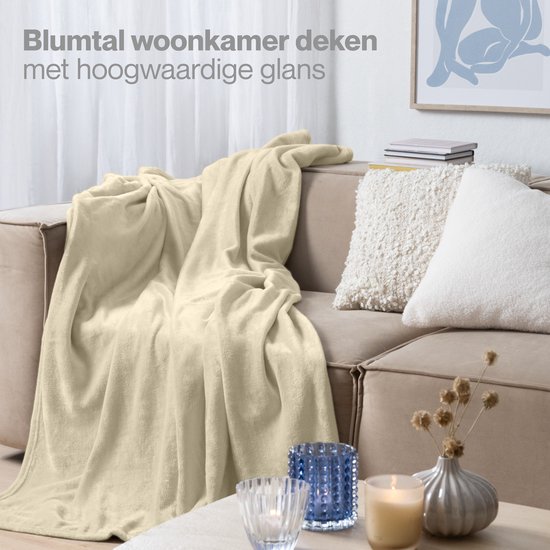 Een zandkleurige Blumtal woonplaid van fleece, losjes over een bank gedrapeerd.