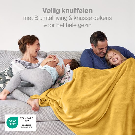 Familie lacht op de bank, bedekt met een gele plaid.