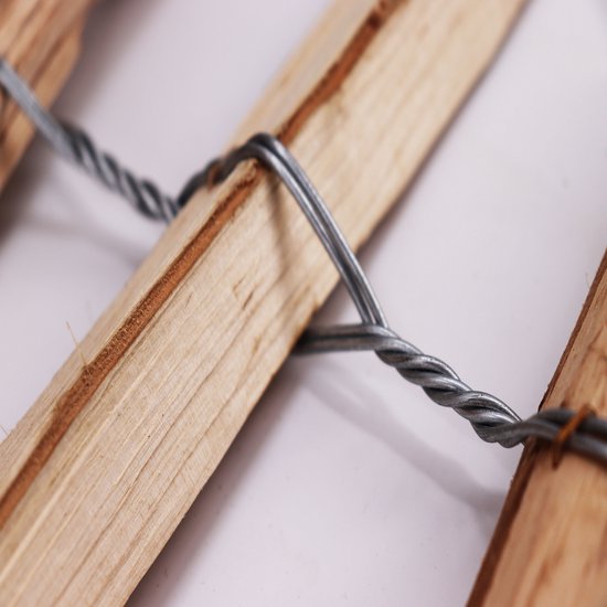 Detail van twee houten palen verbonden door verdraaid metaaldraad. Naturel hout.