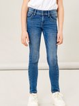 Een meisje draagt een blauwe skinny jeans met witte sneakers, de voorkant van de jeans is zichtbaar.