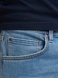 Lichtblauwe jeans met coin pocket en koperkleurige knoop. Deels zichtbaar.