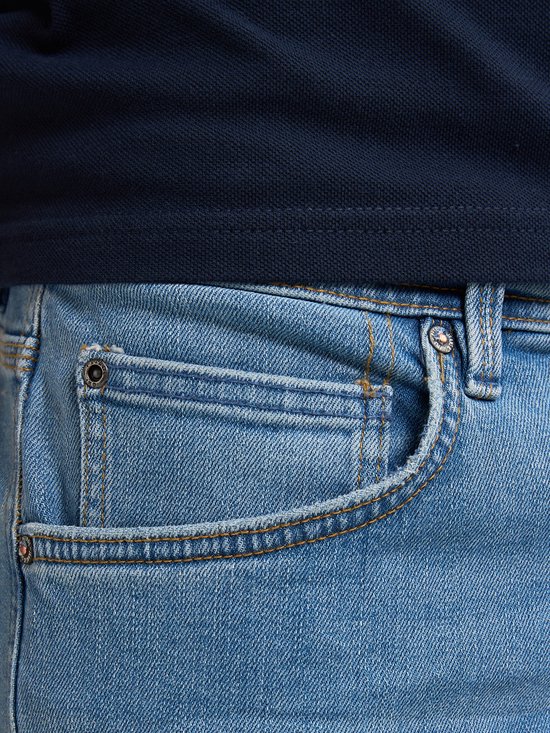 Lichtblauwe jeans met coin pocket en koperkleurige knoop. Deels zichtbaar.