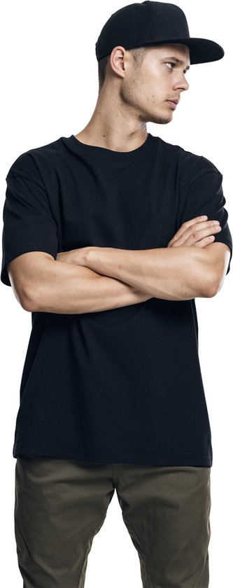 Jonge man met gekruiste armen, draagt een zwart T-shirt en een zwarte pet.