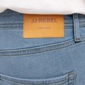 Close-up van een bruin leren label met 'JJ REBEL' op een blauwe jeans.
