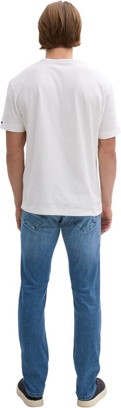 Man met rug naar de camera, draagt een witte T-shirt en blauwe jeans.