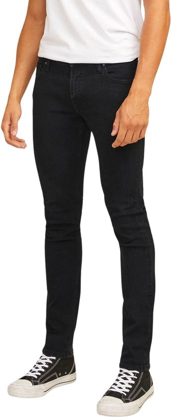 Man in een strakke zwarte jeans en zwarte sneakers, met witte T-shirt.