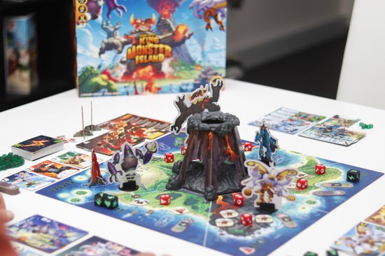Het bordspel 'King of Monster Island' met monsters, dobbelstenen, kaarten en een vulkaan op tafel.