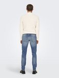 Man met een crème kabeltrui en blauwe jeans, achterkant.