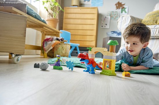 Kind speelt met rode en blauwe T-Rex en groene goblin op vloer.