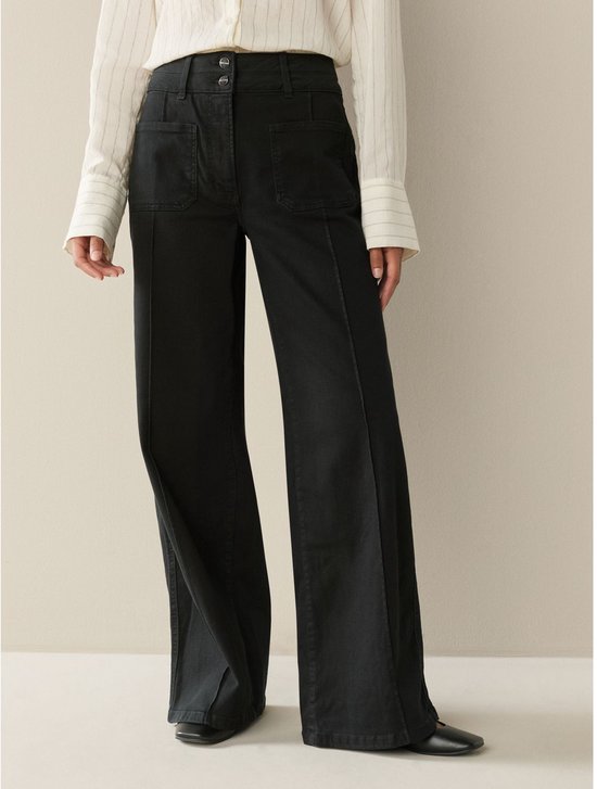Model draagt een zwarte wide leg jeans met hoge taille, gecombineerd met een gestreept hemd.