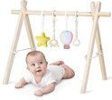 Baby met heldere ogen ligt op de buik onder een houten speelboog met hangend geel sterretje, houten olifant, kleurrijke heteluchtballon en ring.
