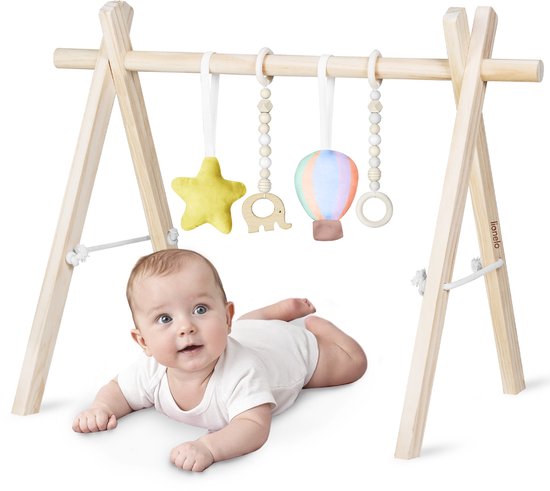 Baby met heldere ogen ligt op de buik onder een houten speelboog met hangend geel sterretje, houten olifant, kleurrijke heteluchtballon en ring.