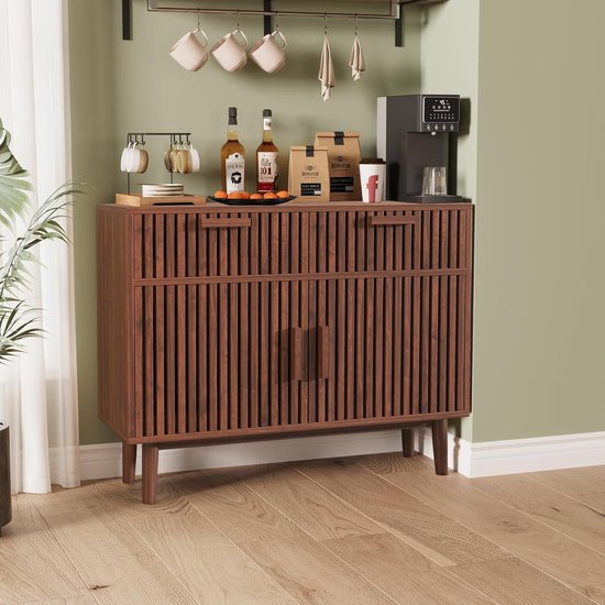 Bruin houten dressoir met verticale lamellen, bekerrekje met mokken, flessen en koffie in de buurt.