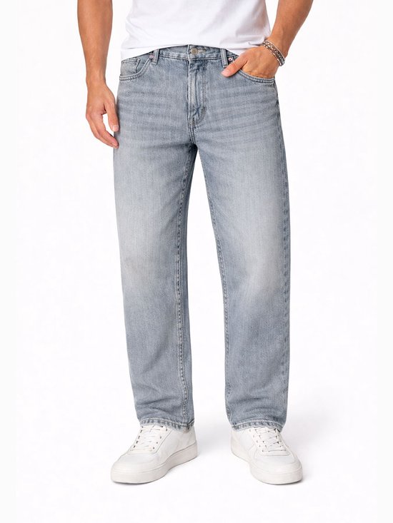 Man in een lichte spijkerbroek met wijdere pijpen. Witte sneakers.