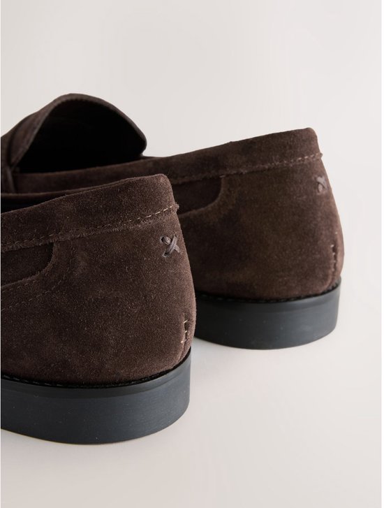 Achterkant van bruine suède loafers met zwarte zolen en stiksels.