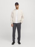 Man met beige bomberjack, wit t-shirt, donkergrijze chino en zwarte pet.