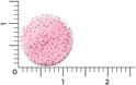 Een enkele roze smelttablet met kleine rode spikkels, afgebeeld naast een liniaal.