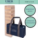 Houten stapeltoren en donkerblauwe draagtas met "TUMBLE TOWER" opdruk en "UBER GAMES" logo's. "HARTHOLZ ARTEN" en "SUPER FEST GESCHLIFFEN" cirkels ernaast.