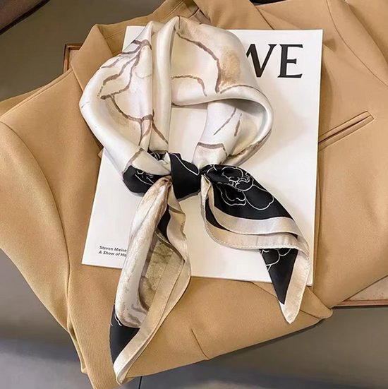 Geknoopte sjaal met crèmekleurige bloemen en zwarte rand, gedrapeerd over een beige blazer.