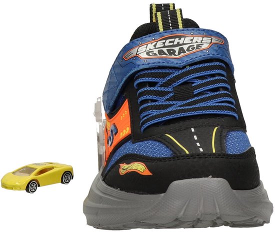 Achterkant van een zwarte sneaker met blauwe en oranje accenten en een kleine gele speelgoedauto.