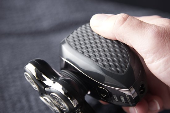 Een hand houdt een zwart Remington hoofdscheerapparaat met geribbelde grip vast.