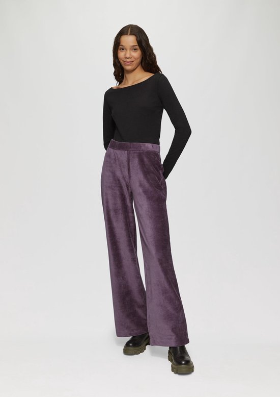 Model in paarse corduroy broek met wijde pijpen en zwarte top.