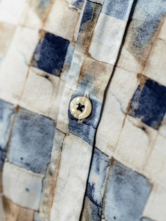Detailopname van een knoop op een overhemd met een blauw en bruin blokpatroon.