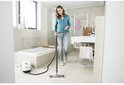 Femme utilisant un nettoyeur vapeur dans une salle de bain carrelée de blanc.