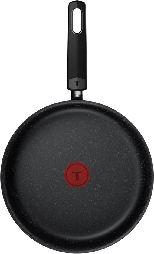 Onderkant van een zwarte koekenpan met rode T-indicator en een gebogen zwart handvat.