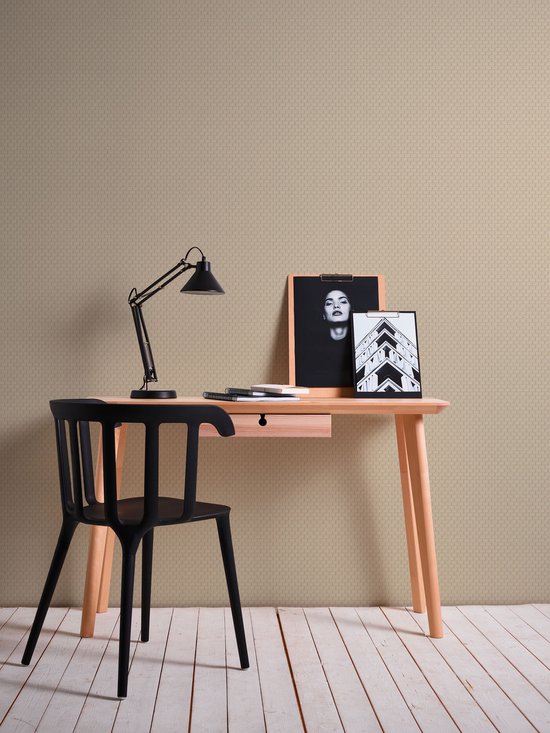 Beige behang met ruitpatroon achter een modern bureau met een zwarte stoel, bureaulamp en fotolijsten.