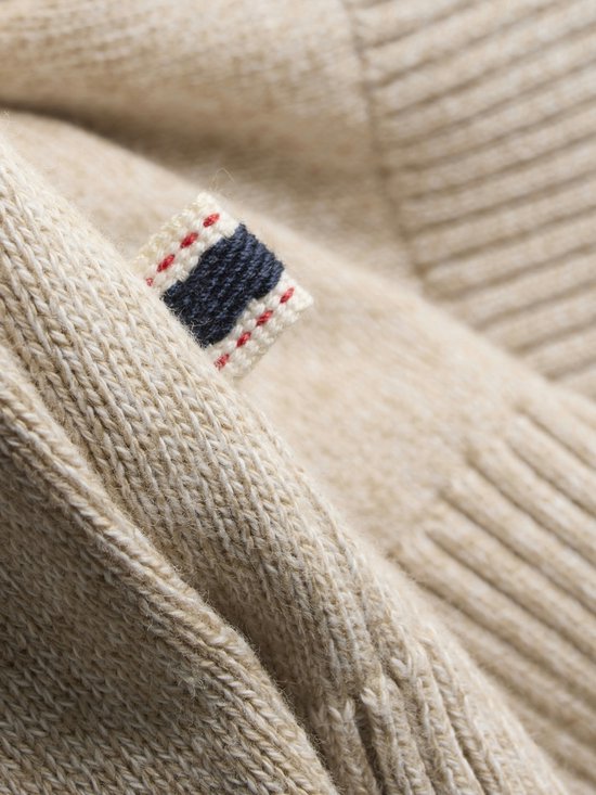 Detail van een beige gebreide stof met een label met blauw, rood en wit.