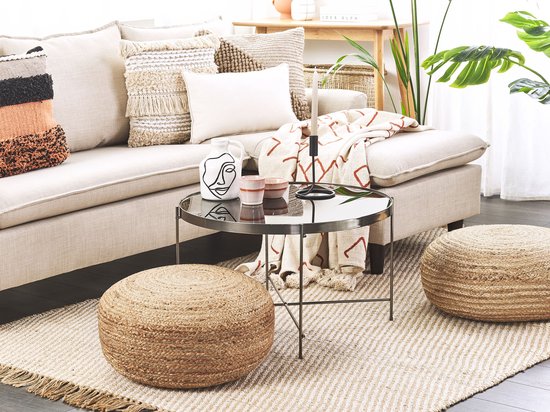 Interieur met een beige bank, een glazen salontafel en twee ronde, handgeweven jute poefen op een tapijt.