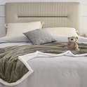 Taupe fleece plaid met witte sherpavoring, gedrapeerd over een bed met een teddybeer.