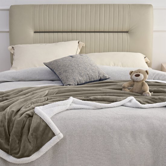 Taupe fleece plaid met witte sherpavoring, gedrapeerd over een bed met een teddybeer.