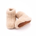 Hoge beige wollen sloffen met zichtbare bruine leren zolen, van de zijkant gezien.