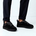 Voeten in donkere broeken en zwarte UGG LO Lowmel sneakers met dikke zolen.