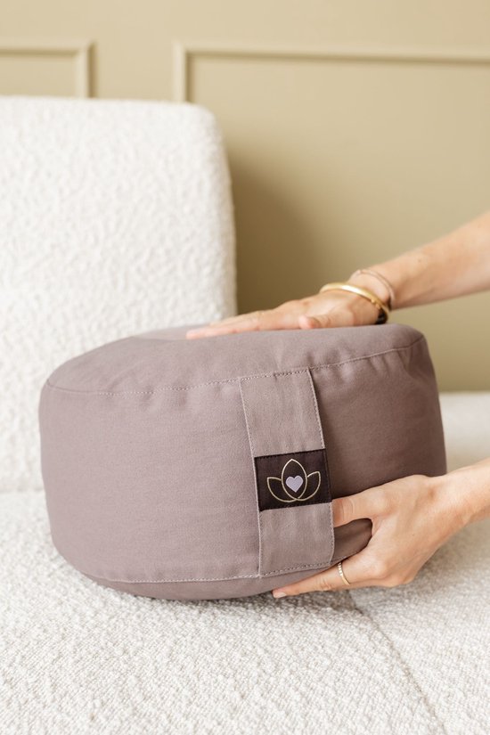 Rond meditatiekussen in taupe kleur, vastgehouden door handen.