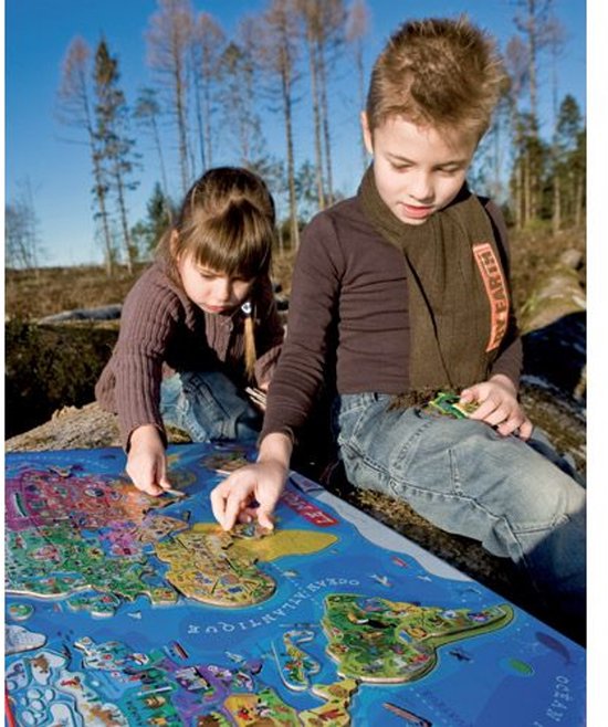 Deux enfants jouent avec un puzzle de carte du monde magnétique, représentant des animaux et des bâtiments.