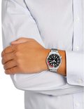 Man met witte blouse en grijze jeans draagt een Citizen duikhorloge om de pols.