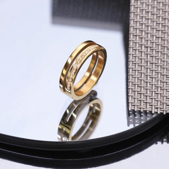 Bague dorée à deux anneaux, ornée de petites pierres claires, sur miroir.