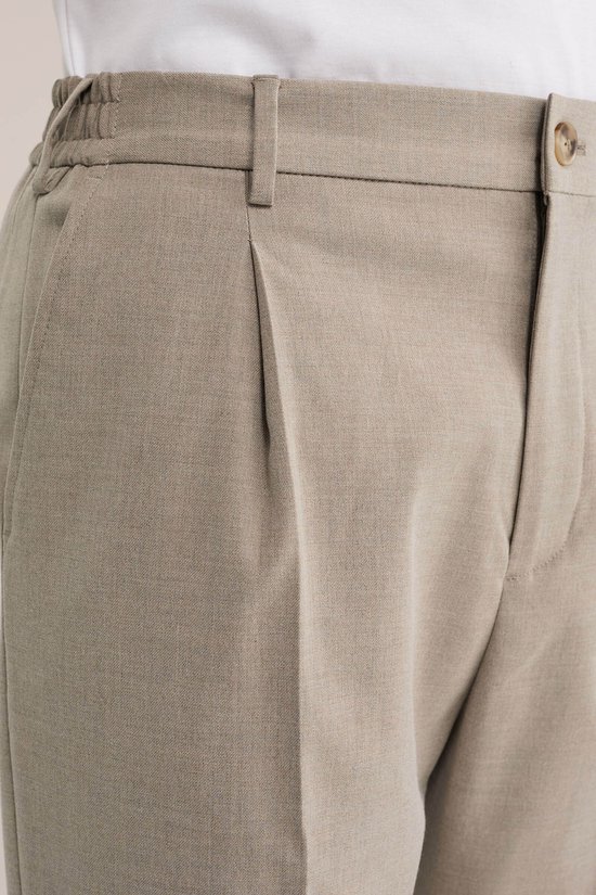 Detail van beige pantalon met bandplooi en elastische tailleband.