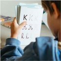 Kind houdt oefenkaart vast met letter K in verschillende schrijfstijlen.