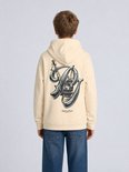 Persoon van achteren gezien in een crèmekleurige hoodie met grote kraan-print en tekst 'Built to Endure'.
