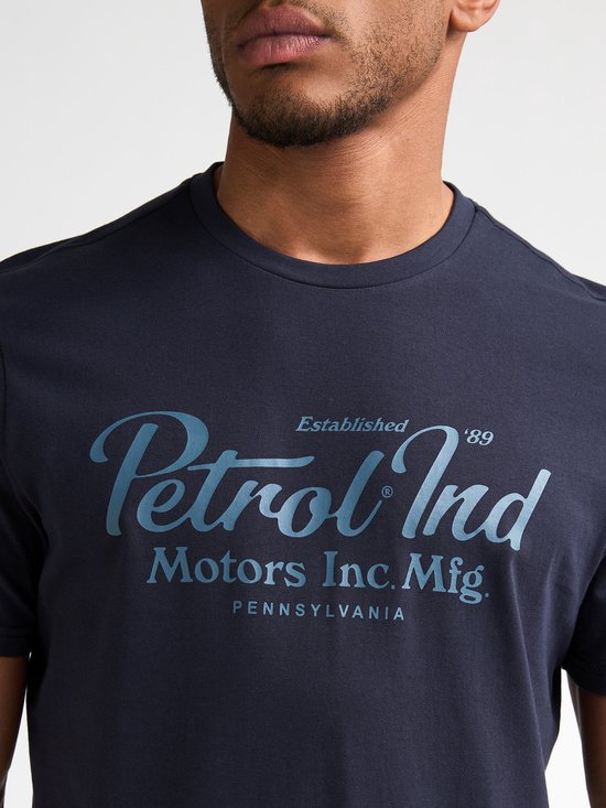 Close-up van een marineblauw T-shirt met een lichtblauwe opdruk van 'Petrol Ind Motors Inc. Mfg. Pennsylvania'.