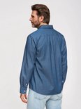 Man met baard, van achteren gezien, draagt een blauw overhemd met witte stipjes en spijkerbroek.
