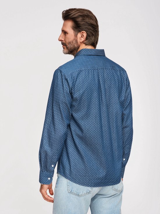Man met baard, van achteren gezien, draagt een blauw overhemd met witte stipjes en spijkerbroek.