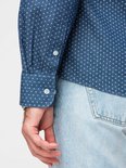 Detail van de manchet en mouw van een blauw overhemd met witte stipjes, knoopsluiting.